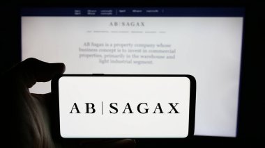 Stuttgart, Almanya - 12-03-2024: İsveçli emlak şirketi AB Sagax 'ın logosuyla cep telefonu sahibi kişi iş sayfasının önünde ekranda. Telefon ekranına odaklan.