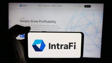 Stuttgart, Almanya - 12-03-2024: ABD 'li finans hizmetleri şirketi IntraFi LLC' nin logosuyla cep telefonu sahibi kişi iş sayfası önünde ekranda. Telefon ekranına odaklan.
