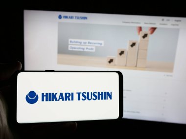 Stuttgart, Almanya - 12-04-2024: Japon şirketi Hikari Tsushin Inc. 'in logosunu elinde tutan kişi web sitesinin önünde ekranda. Telefon ekranına odaklan.
