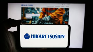 Stuttgart, Almanya - 12-04-2024: Japon şirketi Hikari Tsushin Inc. 'in logosuyla cep telefonu sahibi kişi iş sayfasının önünde ekranda. Telefon ekranına odaklan.