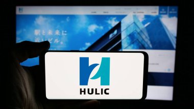 Stuttgart, Almanya - 12-04-2024: Japon emlak şirketi Hulic Co. Ltd. nin logosuyla cep telefonu sahibi kişi iş sayfasının önünde ekranda. Telefon ekranına odaklan.