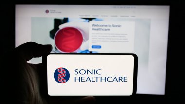 Stuttgart, Almanya - 12-04-2024: Avustralyalı Sonic Healthcare Limited şirketinin logosuyla cep telefonu sahibi kişi iş sayfası önünde ekranda. Telefon ekranına odaklan.