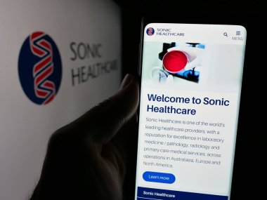 Stuttgart, Germany - 12-04-2024: Person holding cellphone with webpage of Australian company Sonic Healthcare Limited on screen in front of logo. Focus on center of phone display. clipart