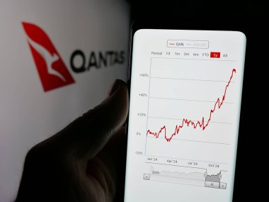 Stuttgart, Almanya - 12-04-2024: Avustralyalı havayolu şirketi Qantas Airways Limited 'in internet sayfası ile cep telefonu tutan kişi logo ile ekranda. Telefon ekranının merkezine odaklan.