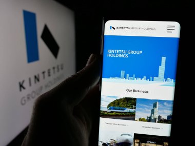 Stuttgart, Almanya - 12-04-2024: Japon şirketi Kintetsu Group Holding Co. Ltd. nin internet sayfası ile cep telefonu tutan kişi logo ile ekranda. Telefon ekranının merkezine odaklan.