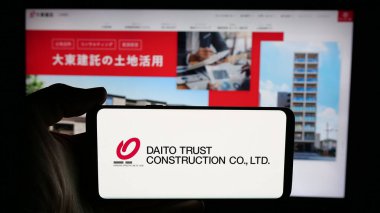 Stuttgart, Germany - 12-04-2024: Person holding cellphone with logo of company Daito Trust Construction Company Ltd. on screen in front of business webpage. Focus on phone display. clipart