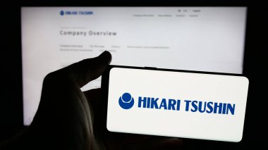 Stuttgart, Almanya - 12-04-2024: Japon firması Hikari Tsushin Inc. 'in logosuyla cep telefonu sahibi kişi iş sayfasının önünde ekranda. Telefon ekranına odaklan.