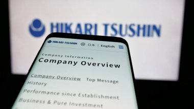 Stuttgart, Germany - 12-04-2024: Smartphone with website of Japanese company Hikari Tsushin Inc. on screen in front of business logo. Focus on top-left of phone display. clipart