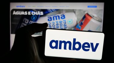 Stuttgart, Almanya - 12-04-2024: Brezilyalı içecek şirketi Ambev S.A. 'nın logosunu taşıyan cep telefonu sahibi kişi iş sayfasının önünde ekranda. Telefon ekranına odaklan.