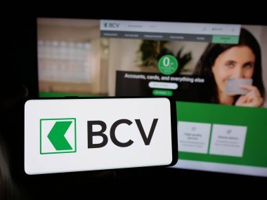 Stuttgart, Germany - 12-04-2024: Person holding smartphone with logo of Swiss company Banque Cantonale Vaudoise (BCV) on screen in front of website. Focus on phone display. clipart