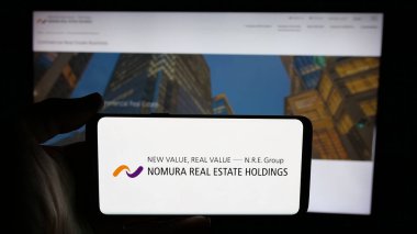 Stuttgart, Germany - 12-05-2024: Person holding cellphone with logo of Japanese company Nomura Real Estate Holdings Inc. on screen in front of webpage. Focus on phone display. clipart