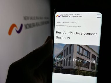 Stuttgart, Almanya - 12-05-2024: Japon şirketi Nomura Emlak Holding Inc. 'nin web sayfası ile akıllı telefonu elinde tutan kişi logolu ekranda. Telefon ekranının merkezine odaklan.