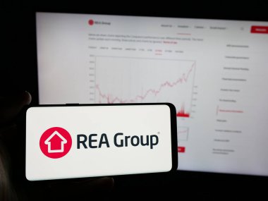 Stuttgart, Almanya - 12-05-2024: Avustralyalı emlak şirketi REA Group Limited 'in logosuna sahip akıllı telefon sahibi kişi web sitesinin önünde ekranda görülüyor. Telefon ekranına odaklan.