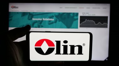Stuttgart, Almanya - 12-09-2024: ABD 'li kimya şirketi Olin Corporation' ın logosuyla cep telefonu sahibi kişi iş sayfasının önünde ekranda. Telefon ekranına odaklan.