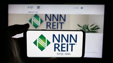 Stuttgart, Almanya - 12-09-2024: ABD 'li emlak şirketi NNN REIT Inc.' in logosuyla cep telefonu sahibi kişi iş sayfasının önünde ekranda. Telefon ekranına odaklan.