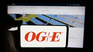 Stuttgart, Almanya - 12-09-2024: Web sayfası önünde ekranda Amerikan şirketi Oklahoma Gas Electric Company 'nin (OGE) logosunun bulunduğu cep telefonu sahibi kişi. Telefon ekranına odaklan.