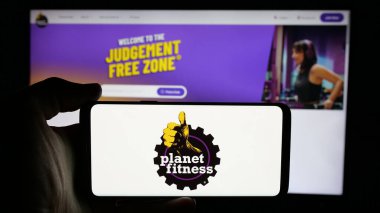 Stuttgart, Almanya - 12-11-2024: ABD 'li spor salonu şirketi Planet Fitness Inc.' in logosuyla cep telefonu sahibi kişi iş sayfasının önünde ekranda. Telefon ekranına odaklan.
