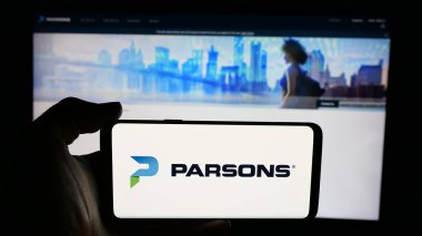 Stuttgart, Germany - 12-11-2024: Person holding cellphone with logo of US engineering company Parsons Corporation on screen in front of business webpage. Focus on phone display. clipart