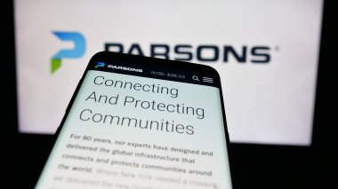 Stuttgart, Germany - 12-11-2024: Mobile phone with website of US engineering company Parsons Corporation on screen in front of business logo. Focus on top-left of phone display. clipart