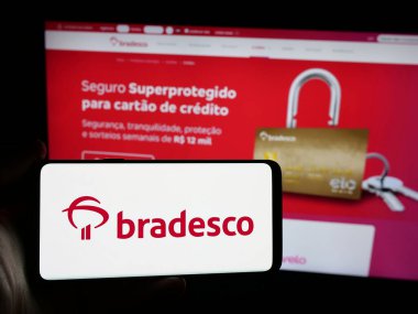 Stuttgart, Almanya - 12-13-2024: Brezilyalı bankacılık şirketi Banco Bradesco SA 'nın logosunu elinde tutan kişi web sitesinin önünde ekranda. Telefon ekranına odaklan.