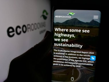 Stuttgart, Almanya - 12-16-2024: EcoRodovias Infraestrutura e Logistica SA şirketinin web sitesi ile cep telefonu tutan kişi logo ile ekranda. Telefon ekranının merkezine odaklan.
