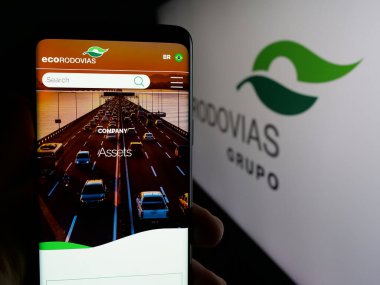Stuttgart, Almanya - 12-16-2024: Ecorodovias Infraestrutura e Logistica SA şirketinin web sayfası ile akıllı telefon sahibi kişi logo ile ekranda. Telefon ekranının merkezine odaklan.