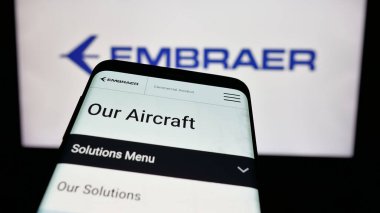 Stuttgart, Almanya - 12-16-2024: Brezilyalı havacılık şirketi Embraer SA 'nın web sitesi ile birlikte iş logosu önünde cep telefonu. Telefon ekranının sol üst kısmına odaklan.