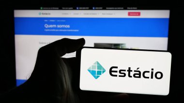 Stuttgart, Almanya - 12-16-2024: Brezilya eğitim şirketi Estacio SA 'nın logosunun bulunduğu cep telefonu sahibi kişi iş sayfasının önünde ekranda. Telefon ekranına odaklan.