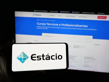 Stuttgart, Almanya - 12-16-2024: Brezilyalı eğitim şirketi Estacio SA 'nın logosunu elinde tutan kişi web sitesinin önünde ekranda. Telefon ekranına odaklan.