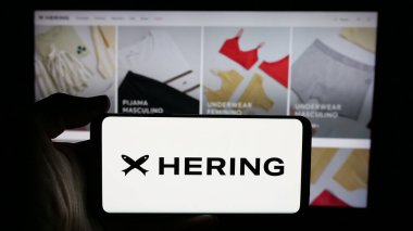 Stuttgart, Almanya - 12-18-2024: Brezilyalı moda şirketi Hering 'in logosunun bulunduğu cep telefonu sahibi kişi iş sayfasının önünde ekranda. Telefon ekranına odaklan.