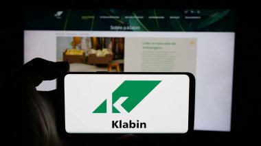 Stuttgart, Almanya - 12-18-2024: Brezilyalı kağıt şirketi Klabin SA 'nın logosuyla cep telefonu sahibi kişi iş sayfasının önünde ekranda. Telefon ekranına odaklan.