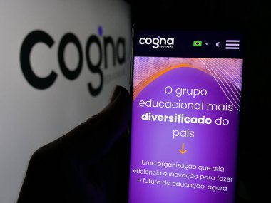 Stuttgart, Almanya - 12-18-2024: Brezilyalı eğitim şirketi Cogna Educacao SA 'nın web sayfası ile logo önünde cep telefonu tutan kişi. Telefon ekranının merkezine odaklan.