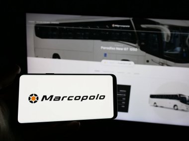 Stuttgart, Almanya - 12-19-2024: Brezilyalı otomotiv şirketi Marcopolo SA 'nın logosunu elinde tutan kişi web sitesinin önünde ekranda. Telefon ekranına odaklan.