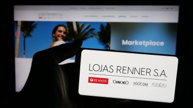 Stuttgart, Almanya - 12-19-2024: Brezilyalı giyim şirketi Lojas Renner SA 'nın logosunu taşıyan cep telefonu sahibi kişi iş sayfasının önünde ekranda. Telefon ekranına odaklan.