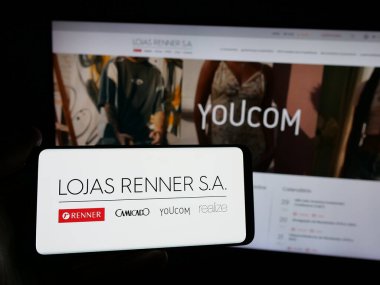 Stuttgart, Almanya - 12-19-2024: Brezilyalı giyim şirketi Lojas Renner SA 'nın logosunun bulunduğu akıllı telefonu web sitesinin önünde tutan kişi. Telefon ekranına odaklan.