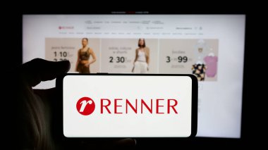 Stuttgart, Almanya - 12-19-2024: Brezilyalı perakende şirketi Renner 'ın logosuyla cep telefonu sahibi kişi iş sayfasının önünde ekranda. Telefon ekranına odaklan.