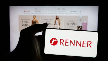 Stuttgart, Almanya - 12-19-2024: Brezilyalı perakende şirketi Renner 'ın logosuyla cep telefonu sahibi kişi iş sayfasının önünde ekranda. Telefon ekranına odaklan.