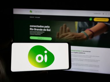 Stuttgart, Almanya - 12-19-2024: Brezilyalı telekomünikasyon şirketi Oi SA 'nın logosunu elinde tutan kişi web sitesi önünde ekranda. Telefon ekranına odaklan.