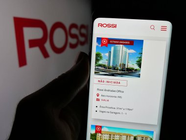 Stuttgart, Germany - 12-19-2024: Person holding cellphone with webpage of Brazilian real estate company Rossi Residencial SA on screen with logo. Focus on center of phone display. clipart