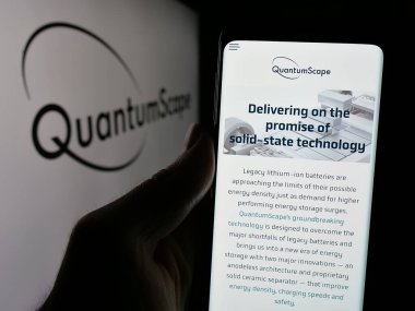 Stuttgart, Germany - 12-20-2024: Person holding cellphone with webpage of US battery company QuantumScape Corporation on screen in front of logo. Focus on center of phone display. clipart