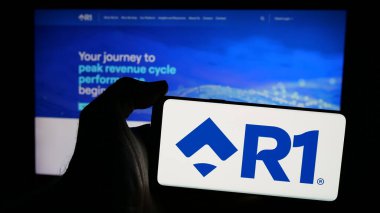 Stuttgart, Almanya - 12-20-2024: Amerikan hasta deneyimi şirketi R1 RCM Inc. 'nin logosunun bulunduğu cep telefonu web sayfası önünde ekranda. Telefon ekranına odaklan.