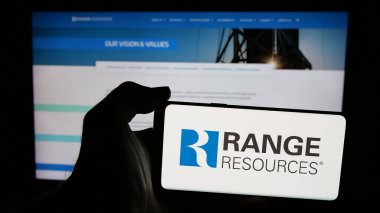 Stuttgart, Germany - 12-20-2024: Person holding mobile phone with logo of US natural gas company Range Resources Corporation on screen in front of web page. Focus on phone display. clipart