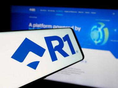 Stuttgart, Germany - 12-20-2024: Mobile phone with logo of American patient experience company R1 RCM Inc. on screen in front of website. Focus on center-left of phone display. clipart