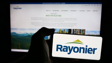 Stuttgart, Almanya - 12-27-2024: Amerikan kereste REIT şirketi Rayonier Inc. 'in logosunu taşıyan cep telefonu sahibi kişi iş sayfasının önünde ekranda. Telefon ekranına odaklan.