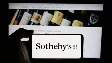 Stuttgart, Almanya - 12-30-2024: İngiliz lüks müzayedeci şirketi Sotheby 'nin logosuna sahip cep telefonu sahibi kişi iş sayfasının önünde ekranda. Telefon ekranına odaklan.