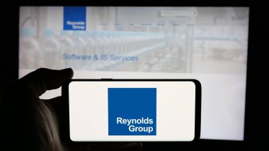 Stuttgart, Germany - 12-30-2024: Person holding cellphone with logo of New Zealand packaging company Reynolds Group Ltd. on screen in front of webpage. Focus on phone display. clipart