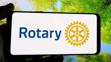 Stuttgart, Germany - 12-30-2024: Person holding cellphone with logo of service club Rotary International on screen in front of website. Focus on phone display. clipart