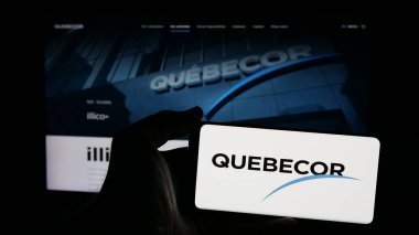 Stuttgart, Germany - 01-02-2024: Person holding mobile phone with logo of Canadian telecommunications company Quebecor Inc. on screen in front of web page. Focus on phone display. clipart