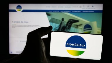 Stuttgart, Almanya - 01-02-2024: Fransız biyoteknoloji şirketi biyoMerieux SA 'nın logosu olan cep telefonu sahibi kişi iş sayfasının önünde ekranda. Telefon ekranına odaklan.