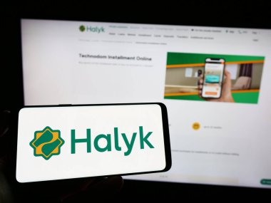 Stuttgart, Almanya - 07-17-2023: Elinde Kazak finans hizmetleri şirketi Halyk Bank 'ın logosunun bulunduğu cep telefonu bulunan kişi web sitesinin önünde ekranda. Telefon ekranına odaklan.